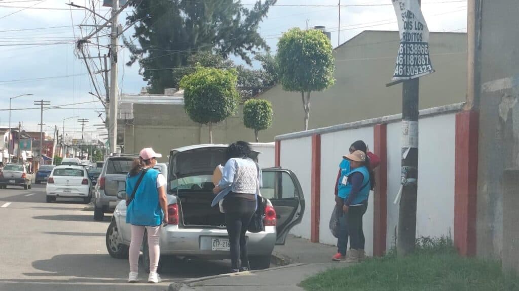 Encuestadores de Morena en Tlaxcala realizan trabajo de campo, mientras un vehículo está estacionado en la calle.