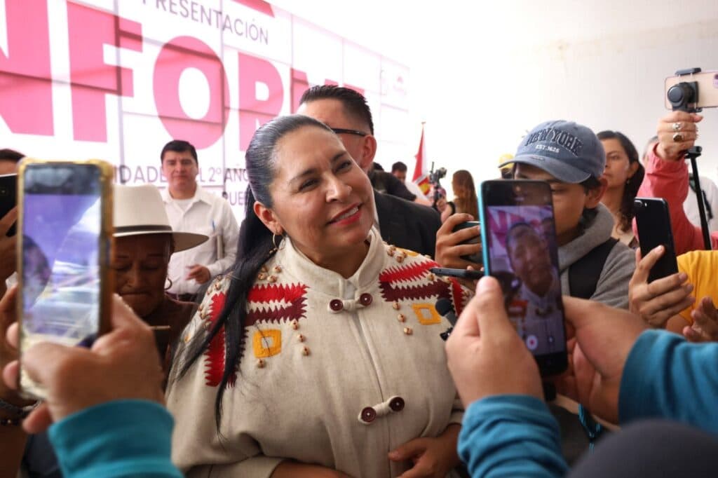 Ana Lilia Rivera Rivera sonríe mientras es rodeada por simpatizantes con teléfonos móviles en un evento político en Tlaxcala.
