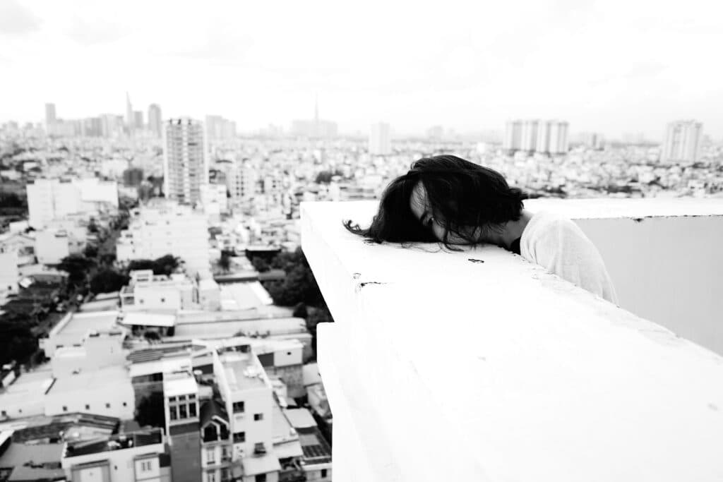 Joven con la cabeza agachada sobre una barandilla, con una vista panorámica de la ciudad de fondo, reflejando la crisis de suicidios en México.